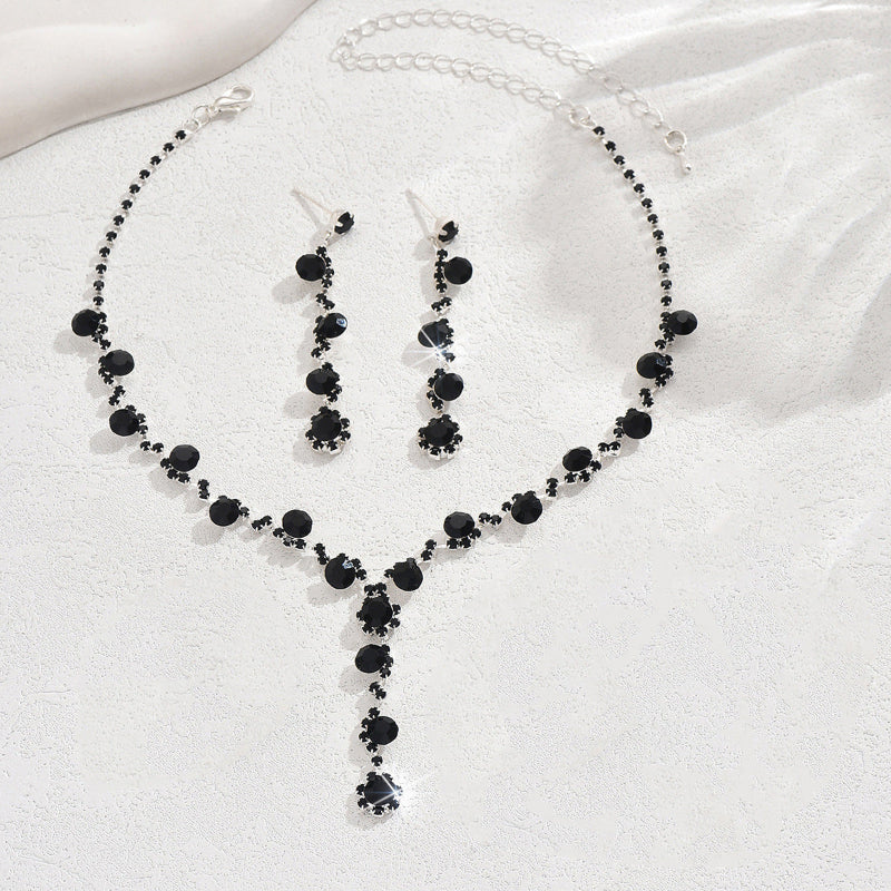 Black beaded necklace and earrings set on a white fabric background