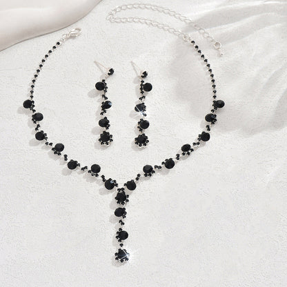 Black beaded necklace and earrings set on a white fabric background
