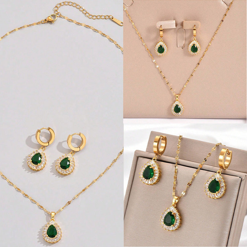 Gold jewelry set with green gemstones on a light gray background