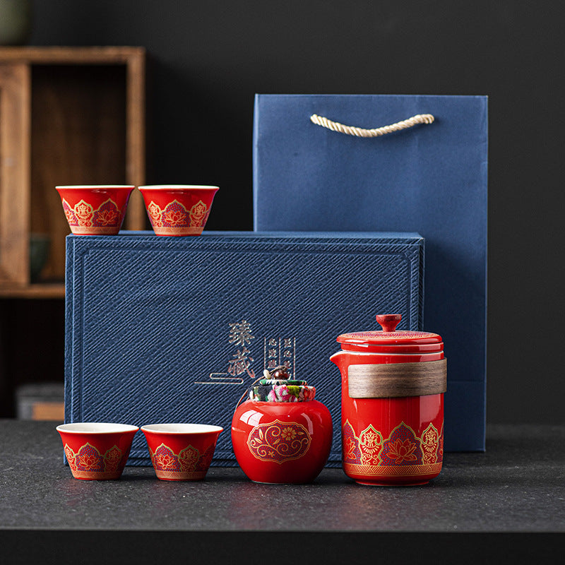 Red ceramic tea set with matching cups and a blue gift box on a dark surface.