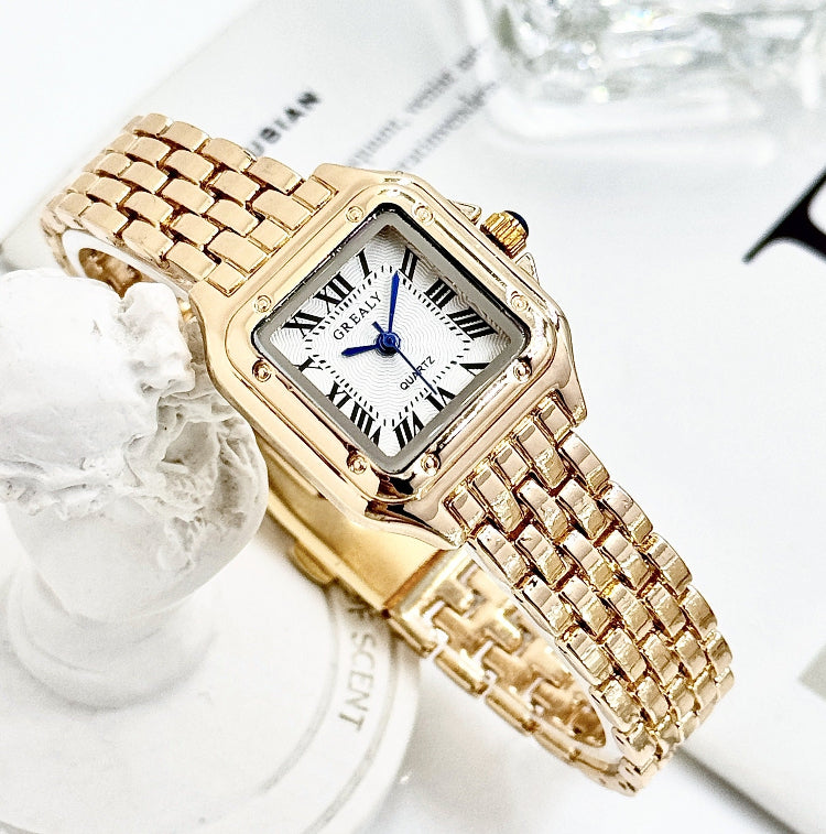 Gold wristwatch with a white face and blue second hand on a decorative surface.