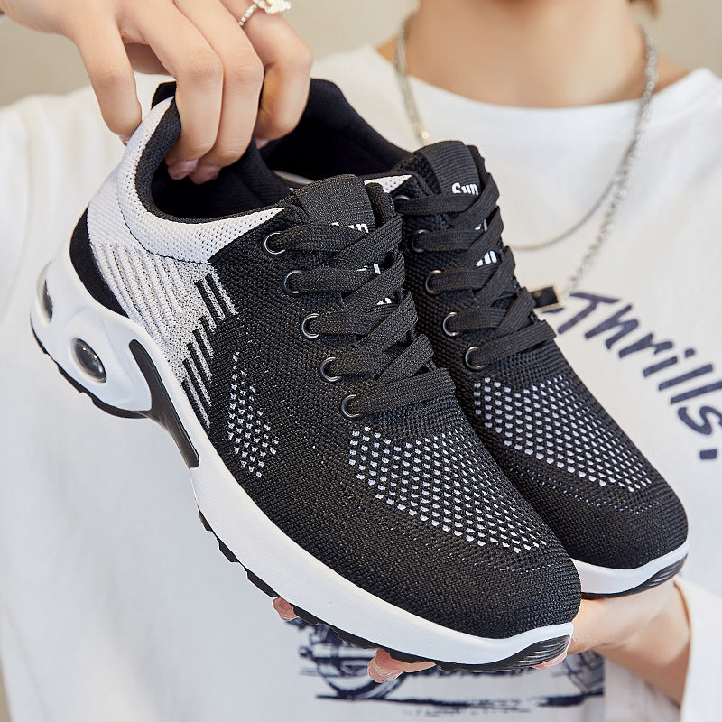 Black and white athletic shoes held by a person against a neutral background