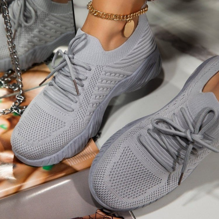 Gray sneakers worn by a person with a gold chain, on a reflective surface.