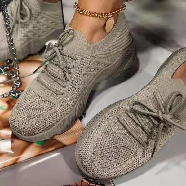 Pair of beige sneakers worn by a person on a reflective surface.