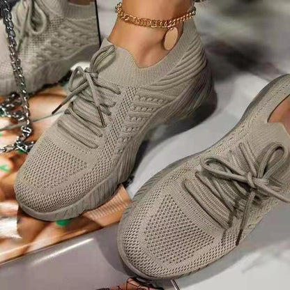 Pair of beige sneakers worn by a person on a reflective surface.