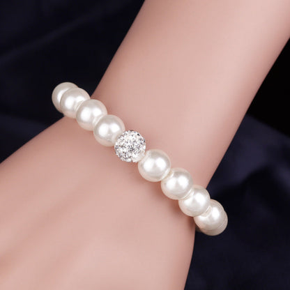 Pearl bracelet with a diamond-like bead on a wrist against a dark background