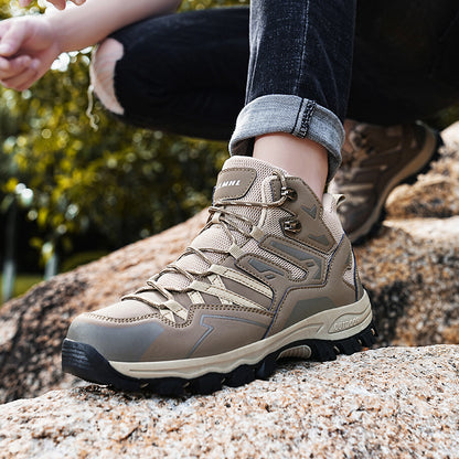 Person wearing beige hiking boots with visible brand name, sitting on a rock outdoors.