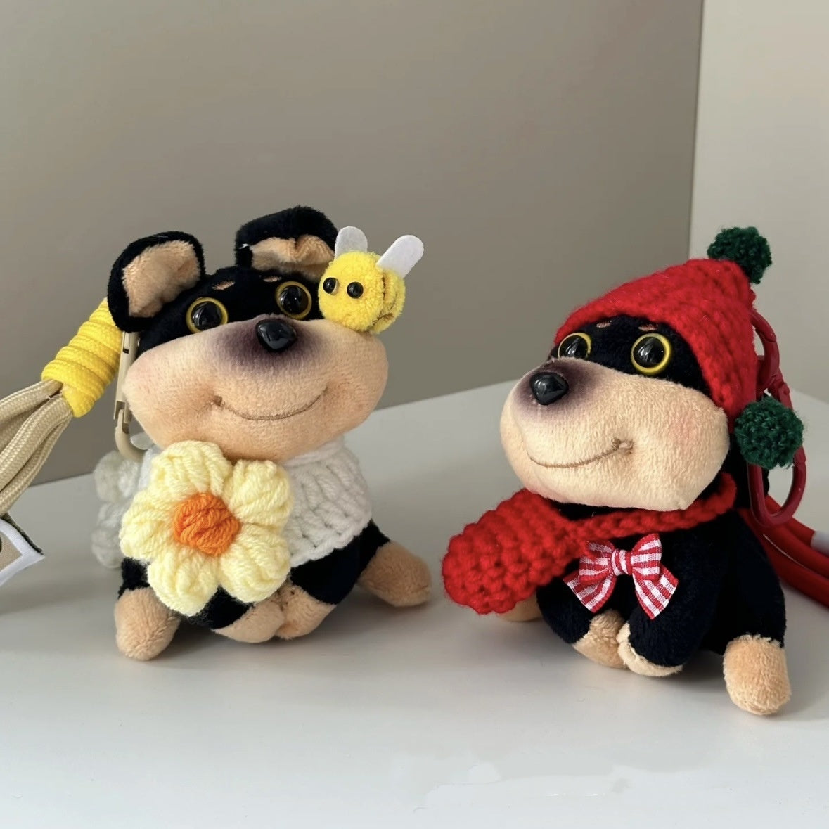 Two plush toys resembling dogs, one in a bee costume and the other in a red outfit with a bow tie, on a neutral background.