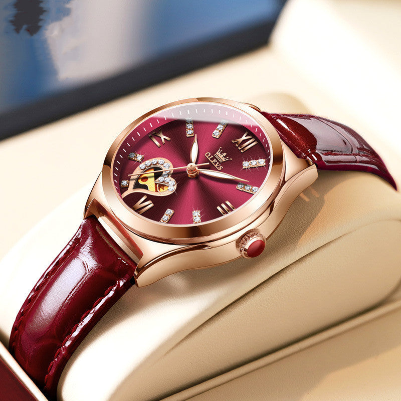 Luxury watch with red face and maroon leather strap on a gold surface