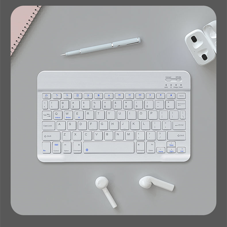 White keyboard on a gray desk with a pen, mouse, and earbuds.
