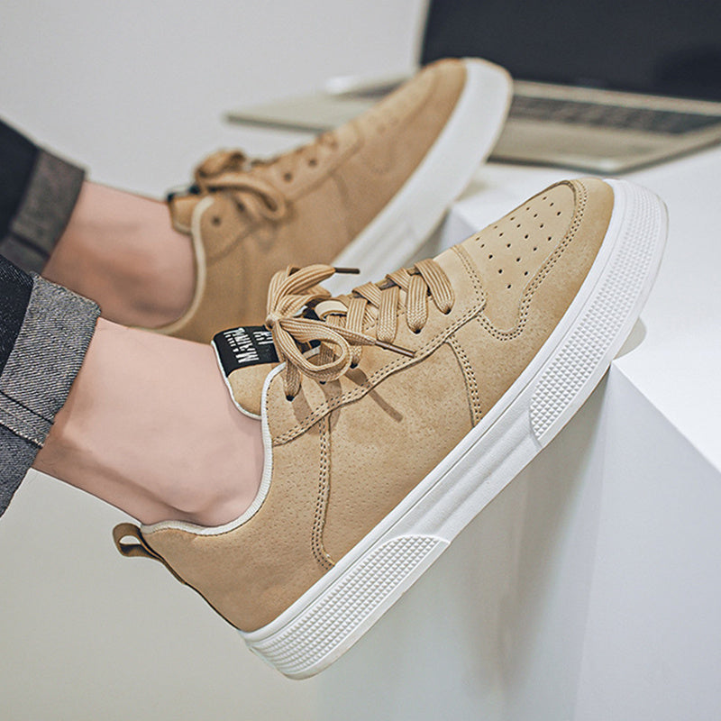 Beige sneakers with white soles worn by a person sitting on a white surface.