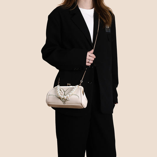 Person holding a pearl-embellished handbag against a beige background