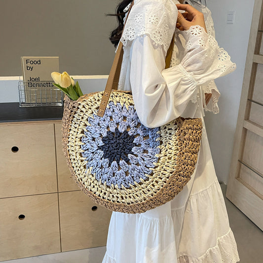 Person holding a round woven bag with a blue floral pattern, wearing a white dress.