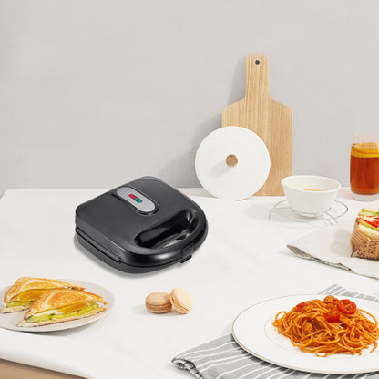 Black sandwich maker on a white table with plates of food and a glass of tea.  YAXSO STORE UAE