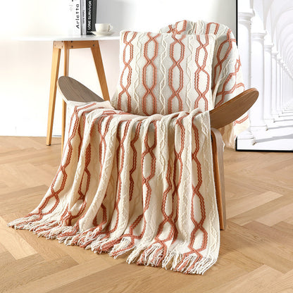 White and orange patterned throw blanket draped over a wooden chair in a room with a table and books.