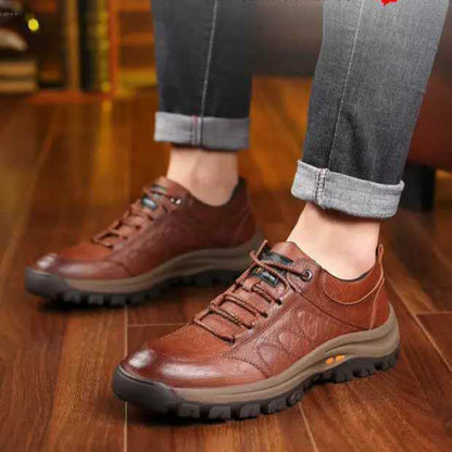 Brown leather shoes worn with rolled-up jeans on a wooden floor.