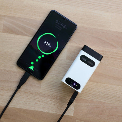 Smartphone with charging cable connected to a white power bank on a wooden surface