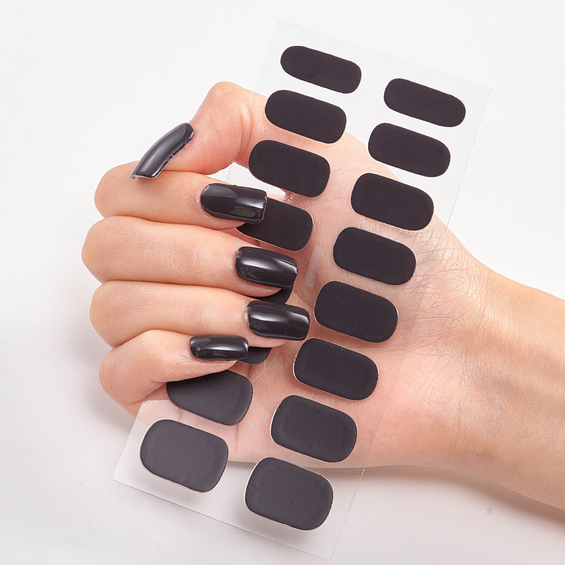 Hand with black nail polish holding a sheet of black nail extensions on a white background