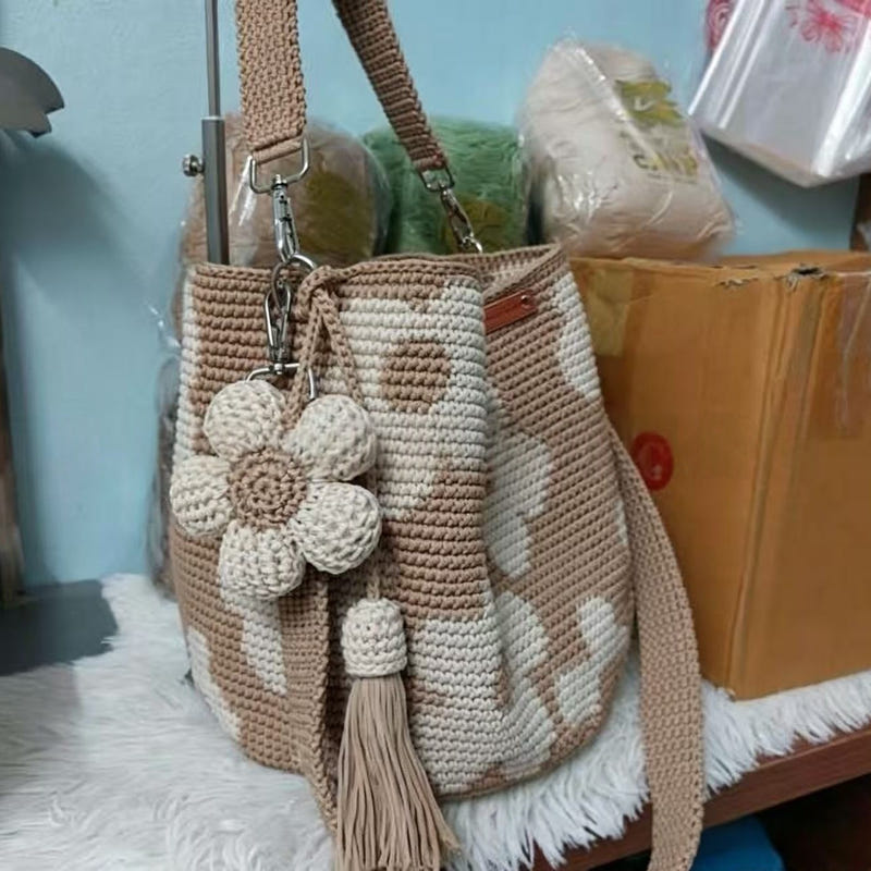 Beige hand-crocheted tote bag with white flowers, drawstring top, and long tassel