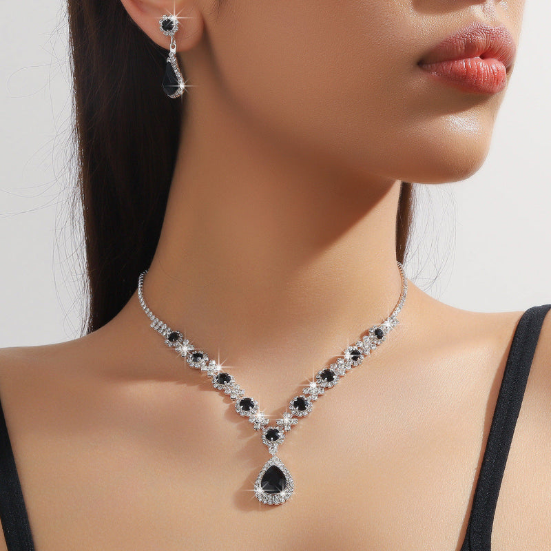 Woman wearing a black and white gemstone necklace and earrings on a plain background