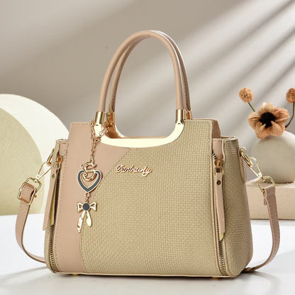 Beige small square crossbody bag with top handles and gold zipper, heart and bow charm