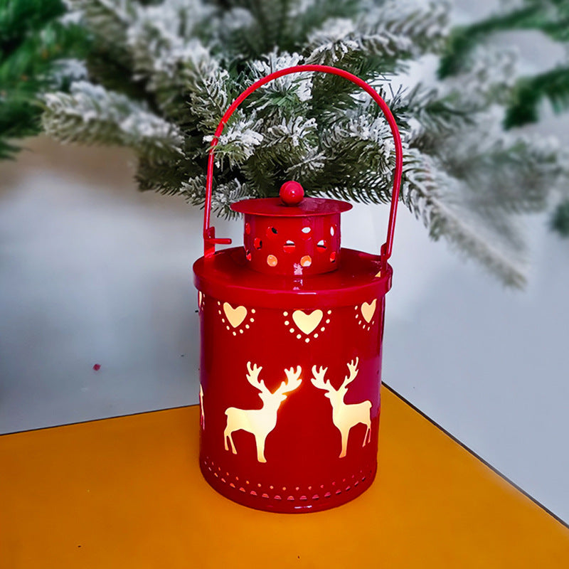 Red lantern with reindeer and heart designs on a yellow surface with a Christmas tree in the background.