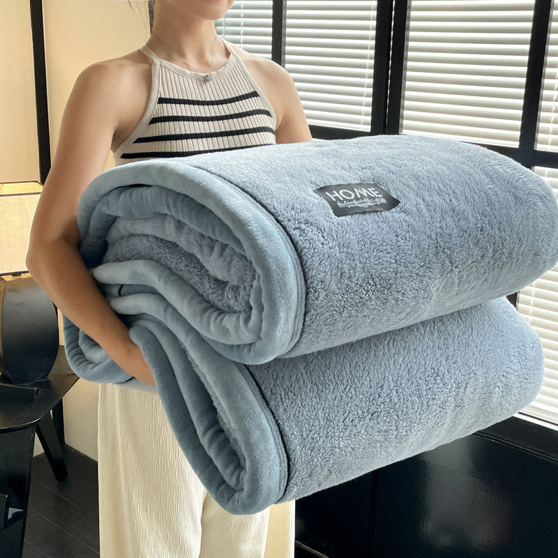 Person holding a light blue blanket with a brand label indoors.