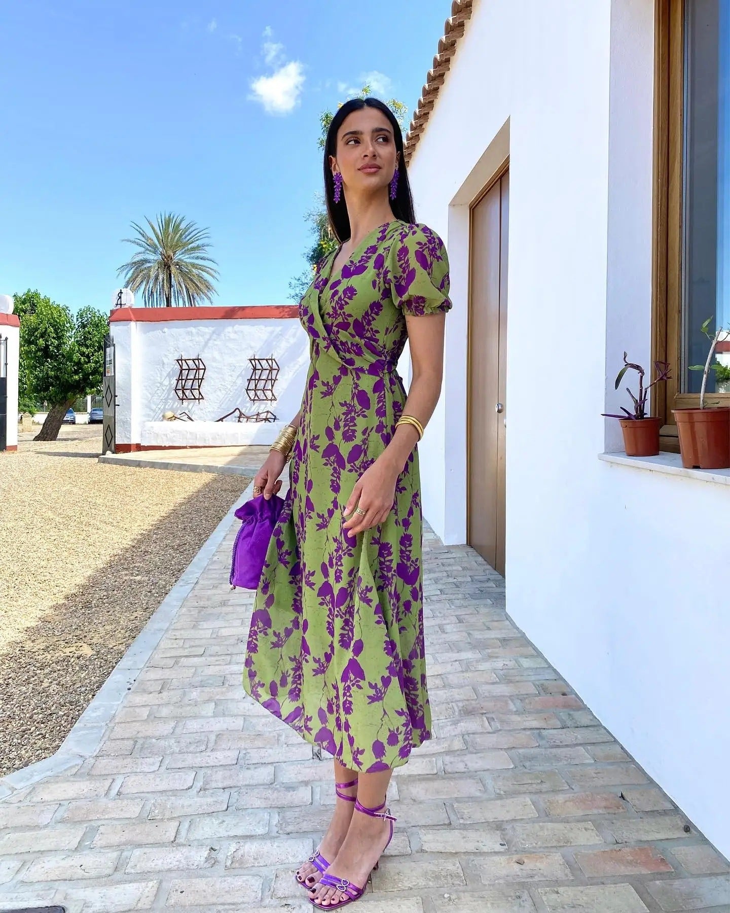 Woman in a green and purple floral dress standing outdoors on a sunny day.