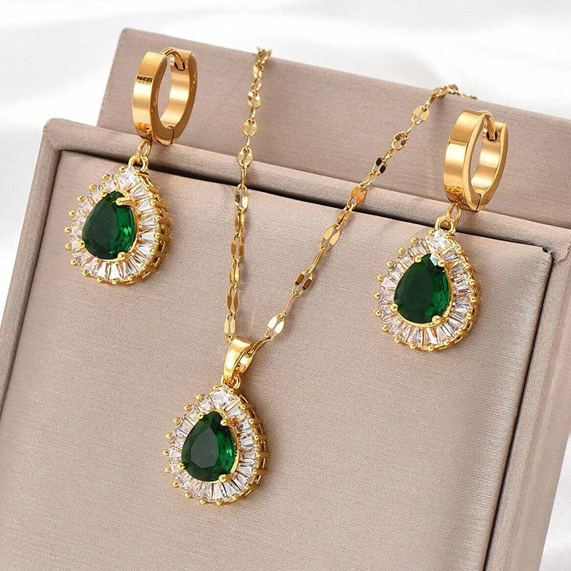 Gold jewelry set with green gemstones on a beige display box