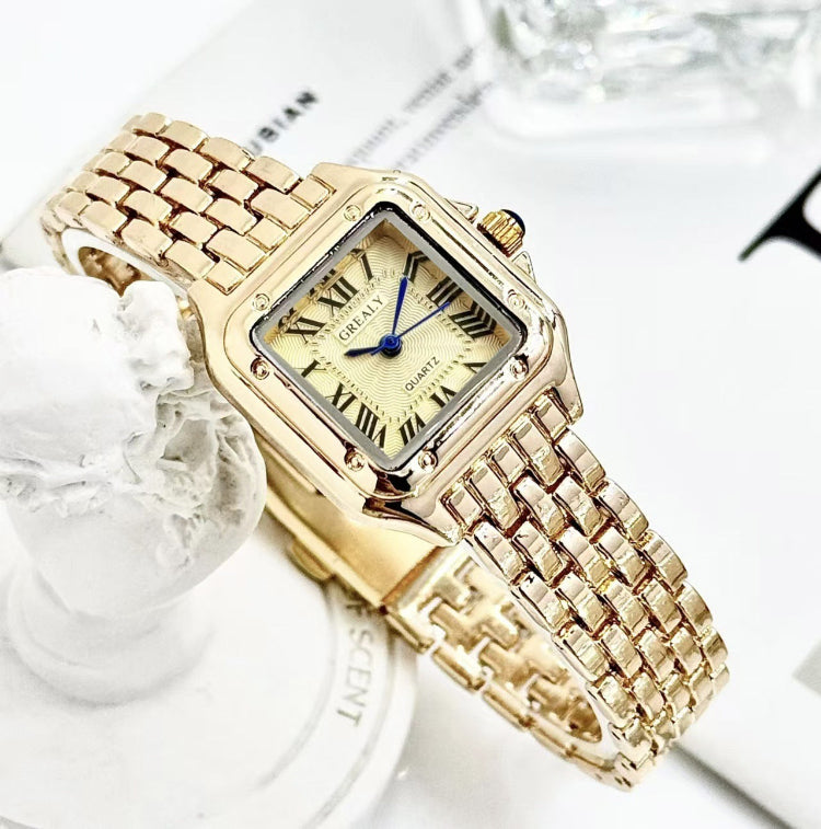 Gold wristwatch with a decorative band on a white background