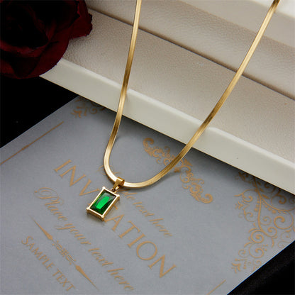 Gold necklace with a green gemstone pendant on a gray surface with gold text.