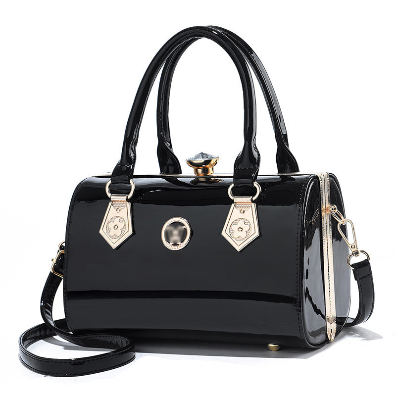 Black patent leather handbag with gold accents on a white background