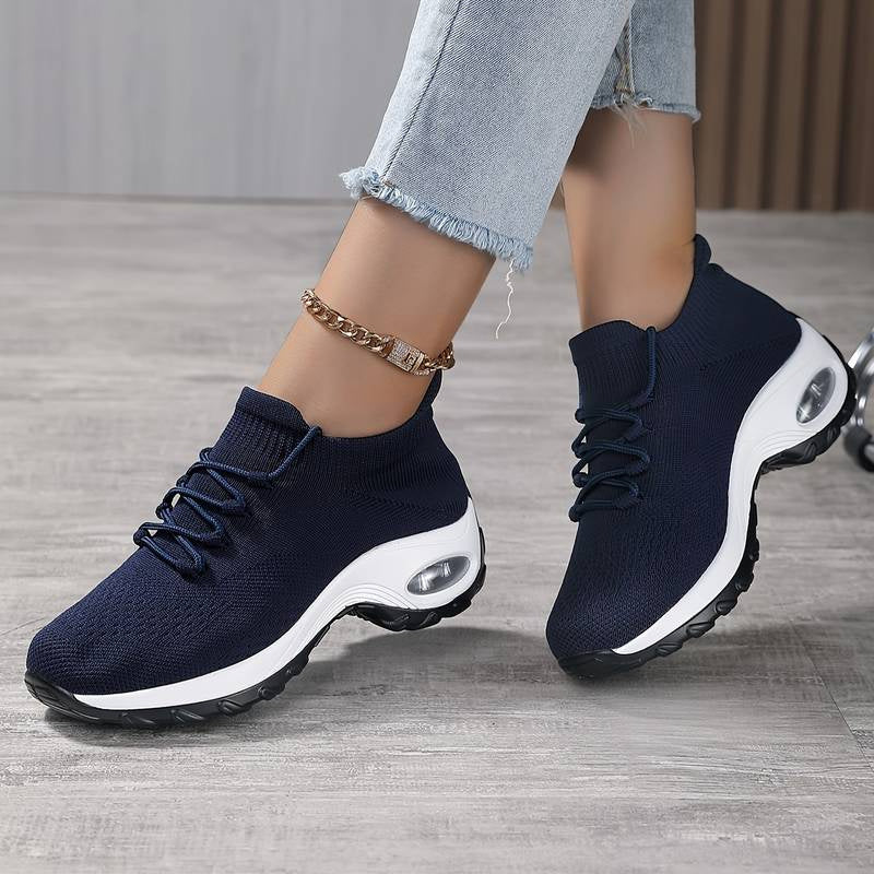 Navy blue athletic shoes with white soles worn by a person on a wooden floor.