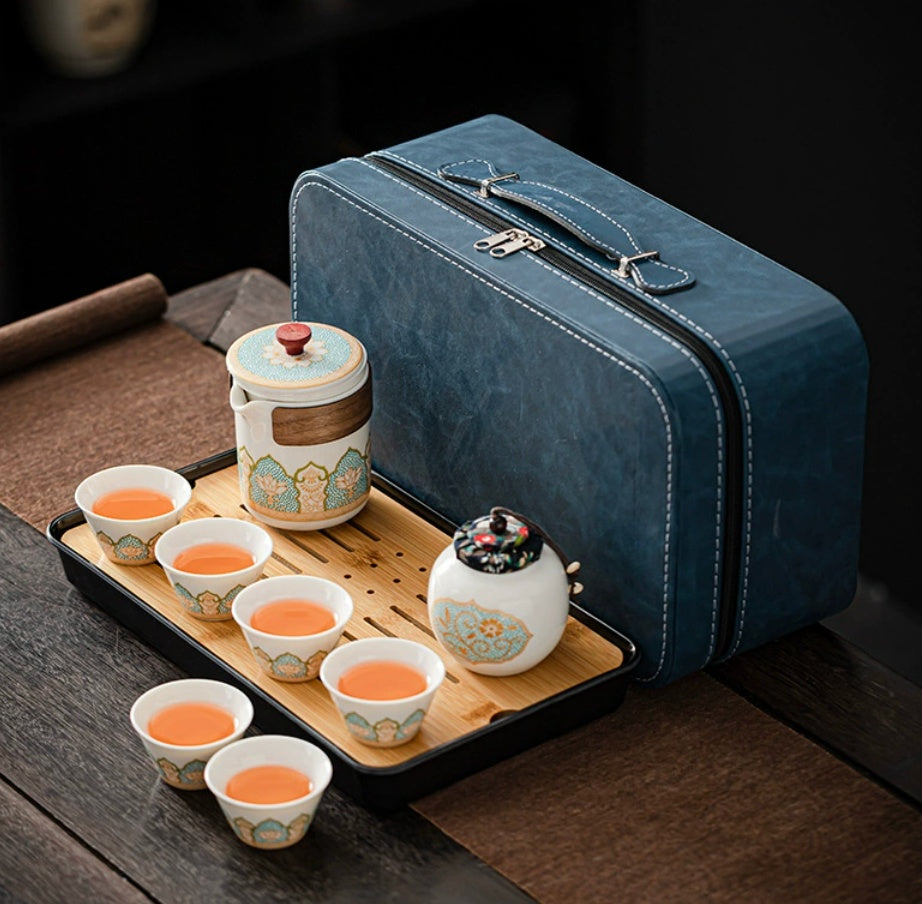 Tea set with ceramic cups and a teapot on a wooden tray next to a blue travel case.
