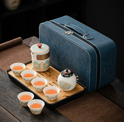 Tea set with ceramic cups and a teapot on a wooden tray next to a blue travel case.