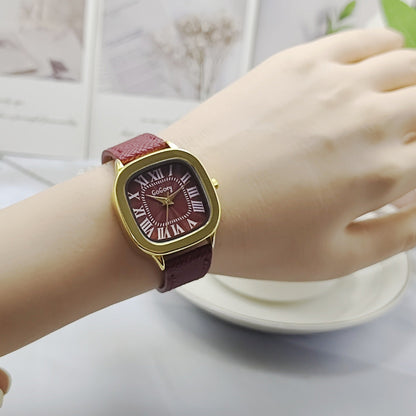 Wrist wearing a watch with a red strap and gold case on a light background