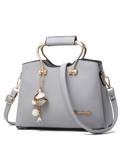 Gray handbag with gold accents and a decorative charm on a white background