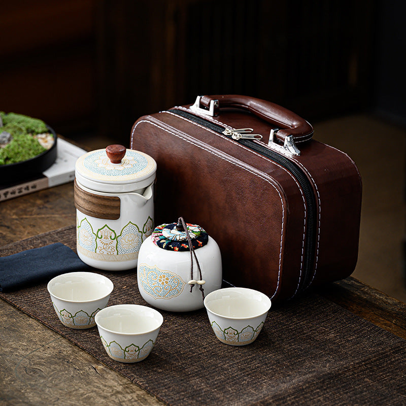 Tea set with ceramic containers and cups on a wooden surface, next to a brown leather suitcase.