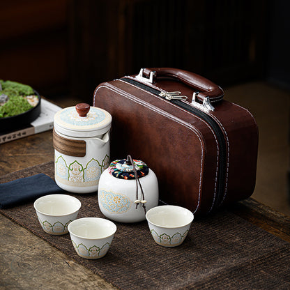 Tea set with ceramic containers and cups on a wooden surface, next to a brown leather suitcase.