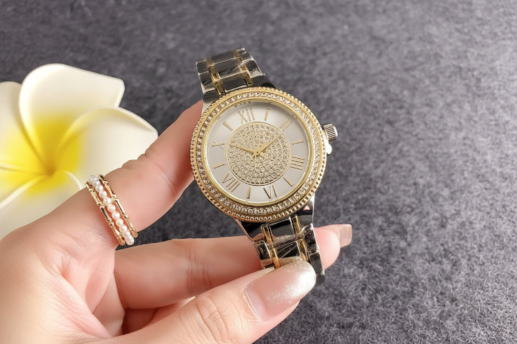 Gold watch with diamond accents held by a hand, with Guess packaging in the background.