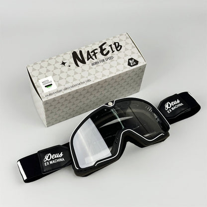 Black goggles with clear lens and black frame, placed in front of a branded box on a light gray background.