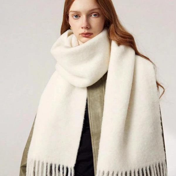Woman wearing a large white scarf with fringe details on a plain background