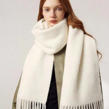 Woman wearing a large white scarf with fringe details on a plain background