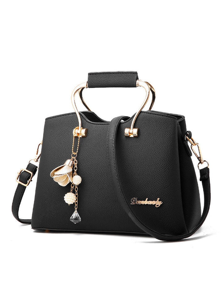 Black handbag with gold accents and floral charm on a white background