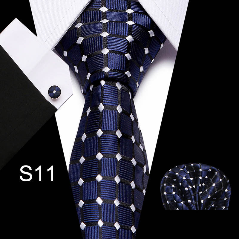 Navy blue tie with white patterns, pocket square, and cufflink on a white shirt.
