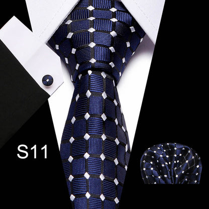 Navy blue tie with white patterns, pocket square, and cufflink on a white shirt.