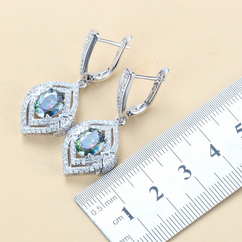 Silver earrings with gemstones next to a ruler on a beige background