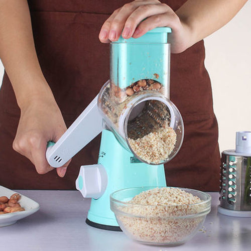 Person using a turquoise manual grinder to make breadcrumbs with a bowl of breadcrumbs on a table.