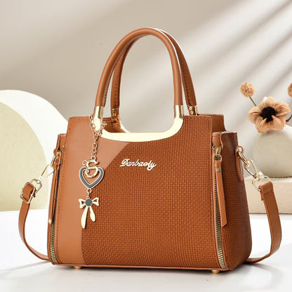 Tan/brown small square crossbody bag with top handles and gold zipper, heart and bow charm