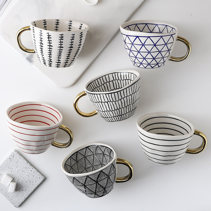 Set of six patterned mugs with gold handles on a white surface